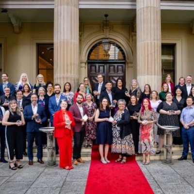 A group of UQ researchers holding award trophies standing out the front of a sandstone building on a red carpet